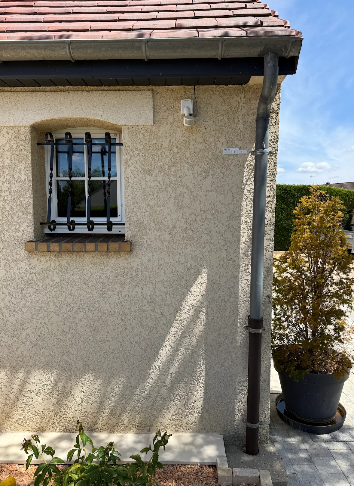 Angle d'une maison crépie avec une gouttière verticale ; une fissure verticale suit le chaînage d'angle.