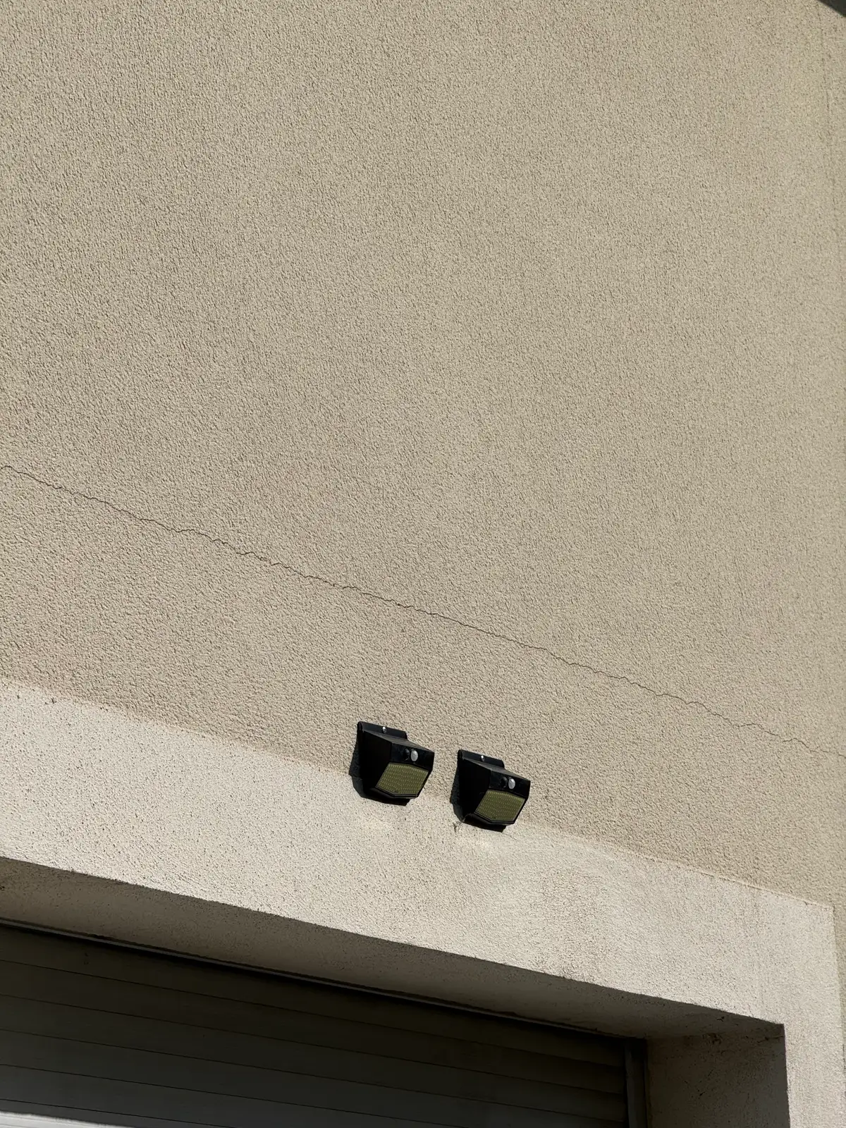 Mur enduit avec une fissure fine et presque horizontale, au-dessus de deux petits projecteurs.